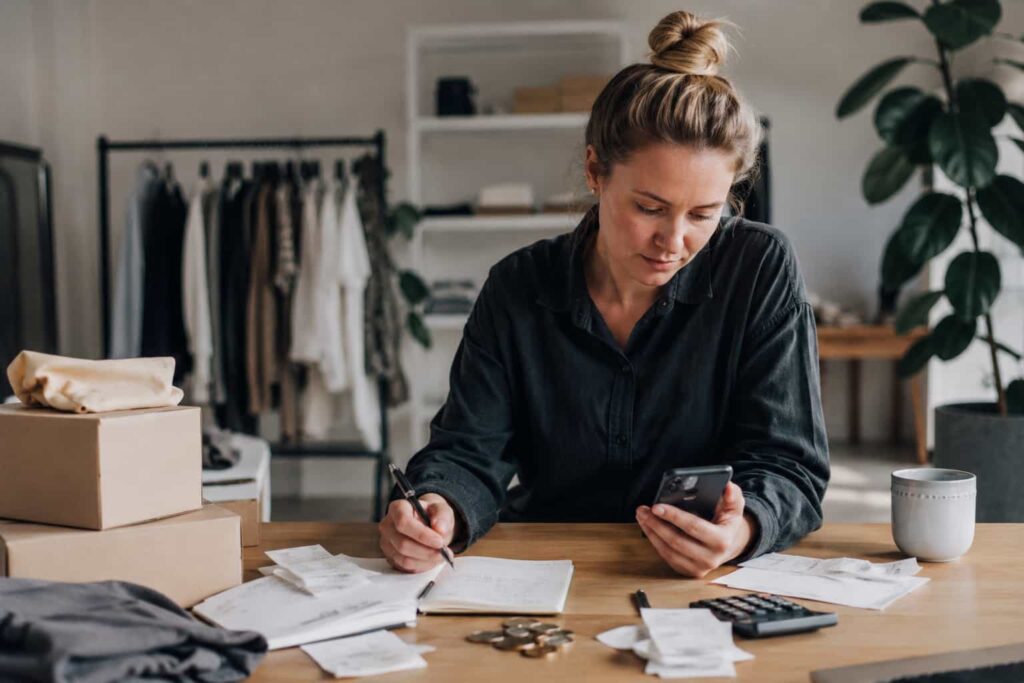 Kvindelig webshop-ejer pakker produkter i et minimalistisk lager- og pakkemiljø med fokus på e-commerce, ordrebehandling og drift af webshop.